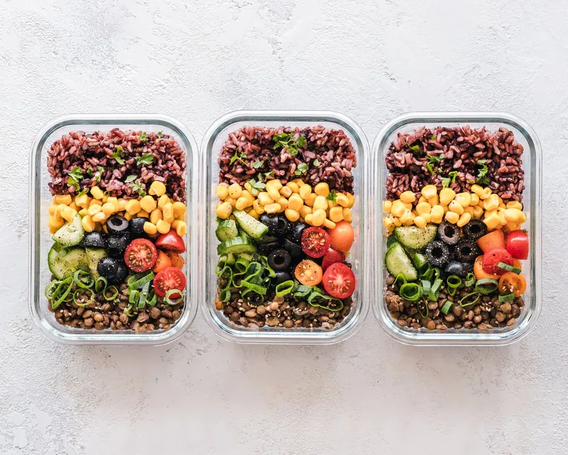 Tres táperes de cristal con lentejas, arroz rojo, maíz, aceitunas negras y tomate cherry