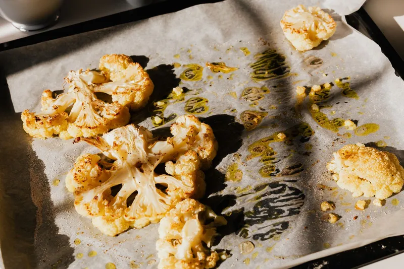 Filetes de coliflor asados sobre papel de horno con un hilo de aceite de oliva en la bandeja