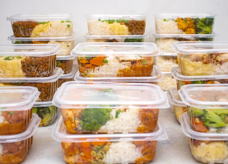 Raciones individuales de arroz con verduras apiladas en recipientes herméticos