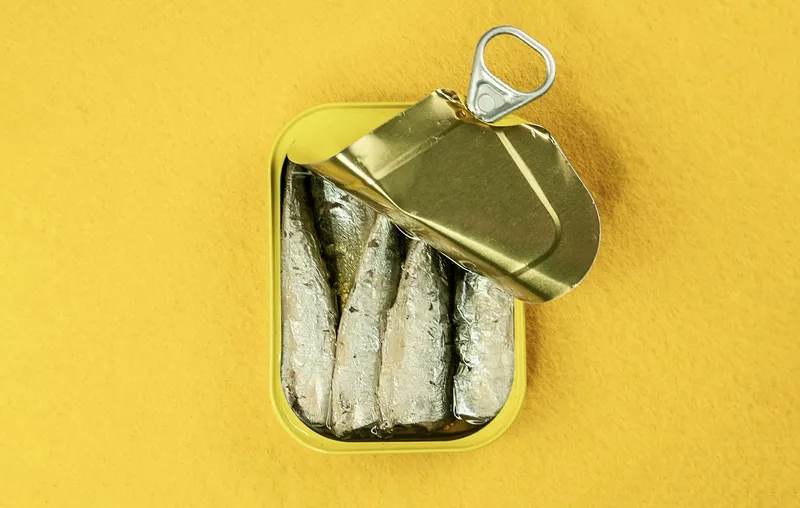 Lata de sardinas en aceite abierta sobre fondo amarillo