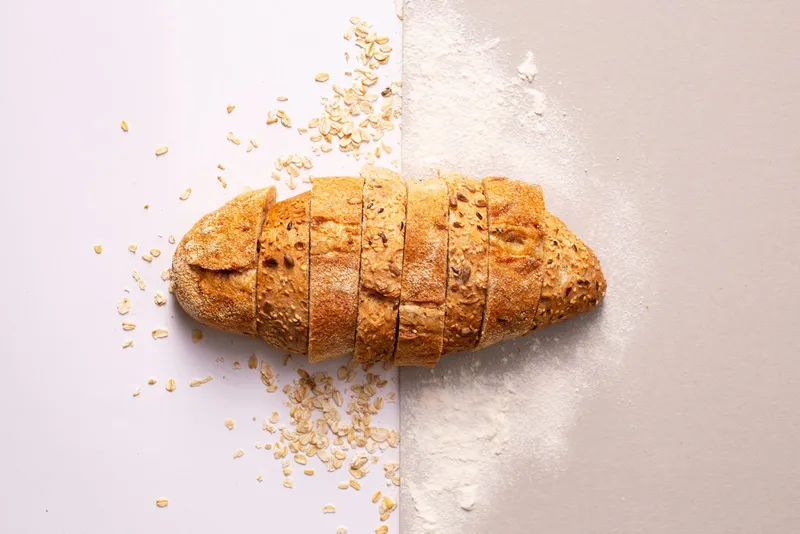 Pan integral con semillas cortado en rebanadas junto a copos de avena